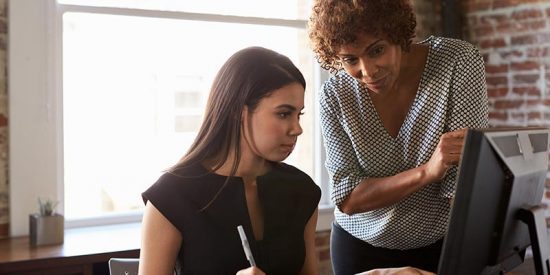 Two businesswomen in an office working together on a computer.