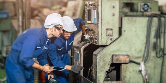 Maintenance workers inspect a machine on a factory floor.