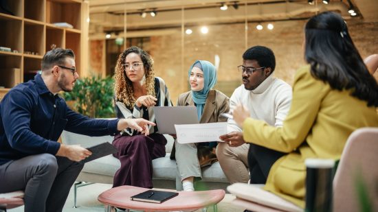 Four diverse employees sit around a table discussion their work.